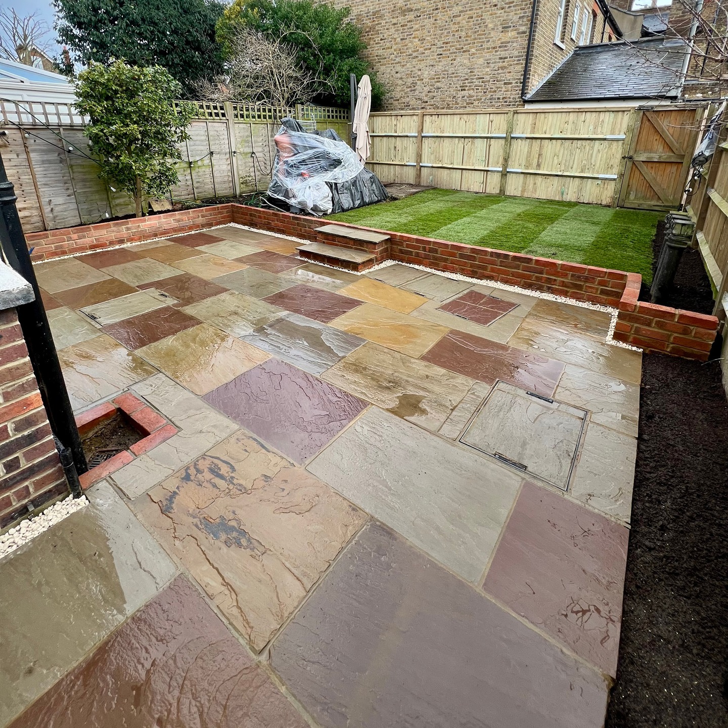 Indian sandstone patio with brick retaining walls and steps up to a new lawn after a full garden rebuild