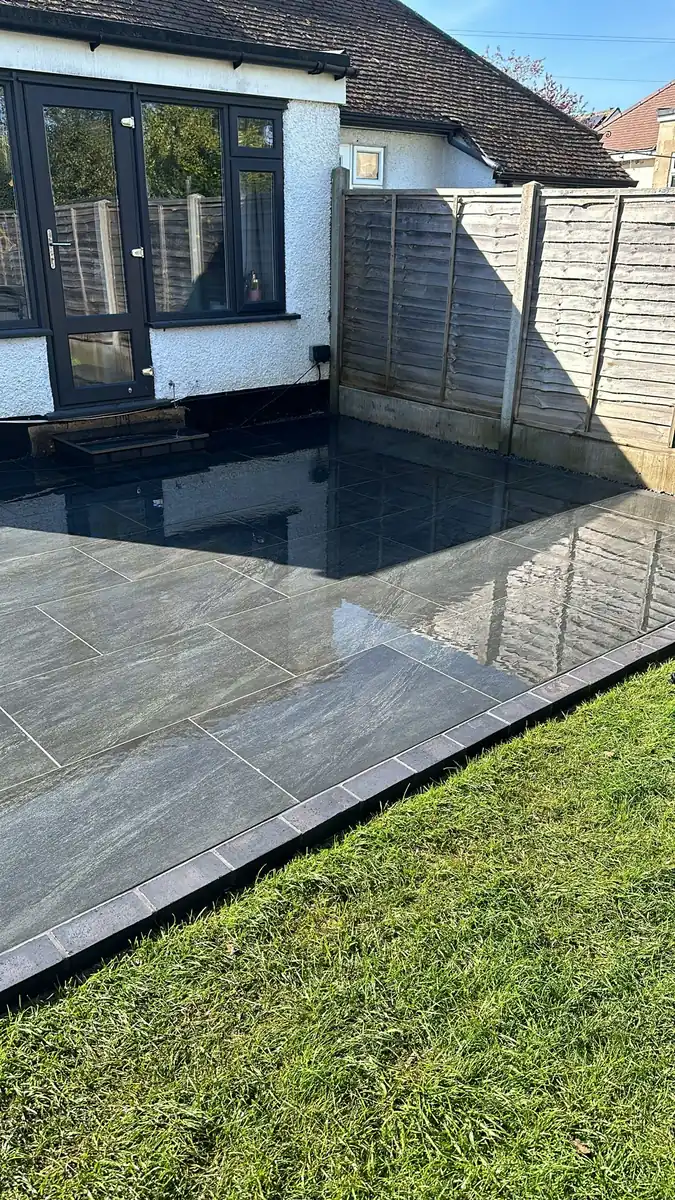 After: dark porcelain patio across the back of the house with a brick edge against the lawn