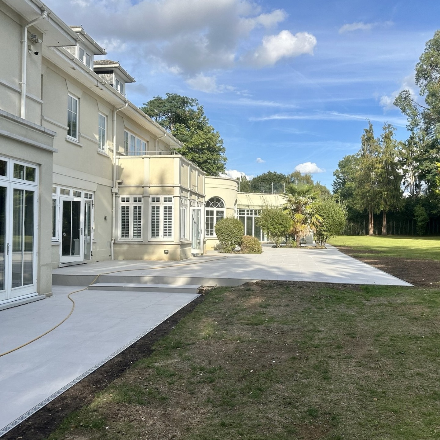 Porcelain terrace stepping down to the lawn at an Oxshott garden, showing the set out and levels