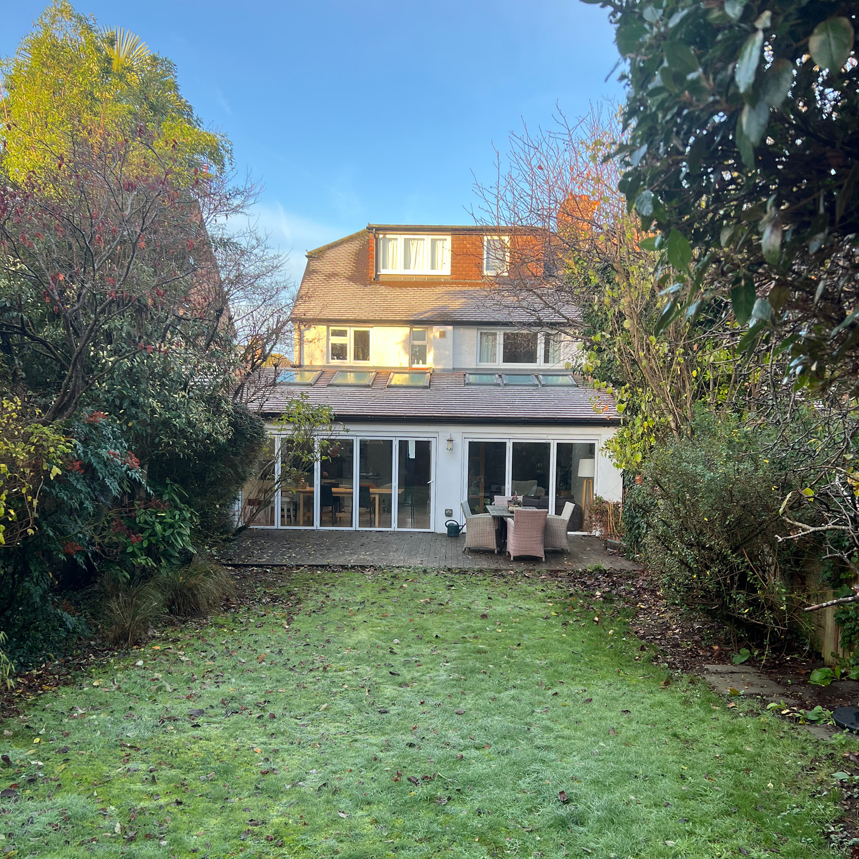 Before: worn grey timber decking and a leaf-covered lawn behind an East Molesey house