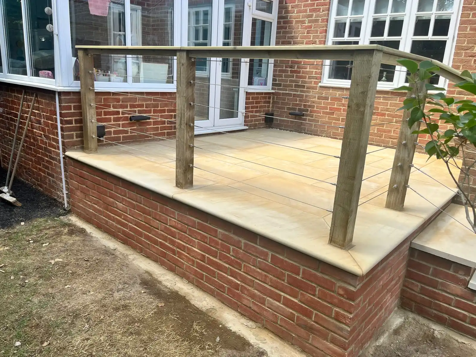 Raised sawn sandstone patio on a red brick retaining wall with a timber and wire balustrade in Esher, Surrey