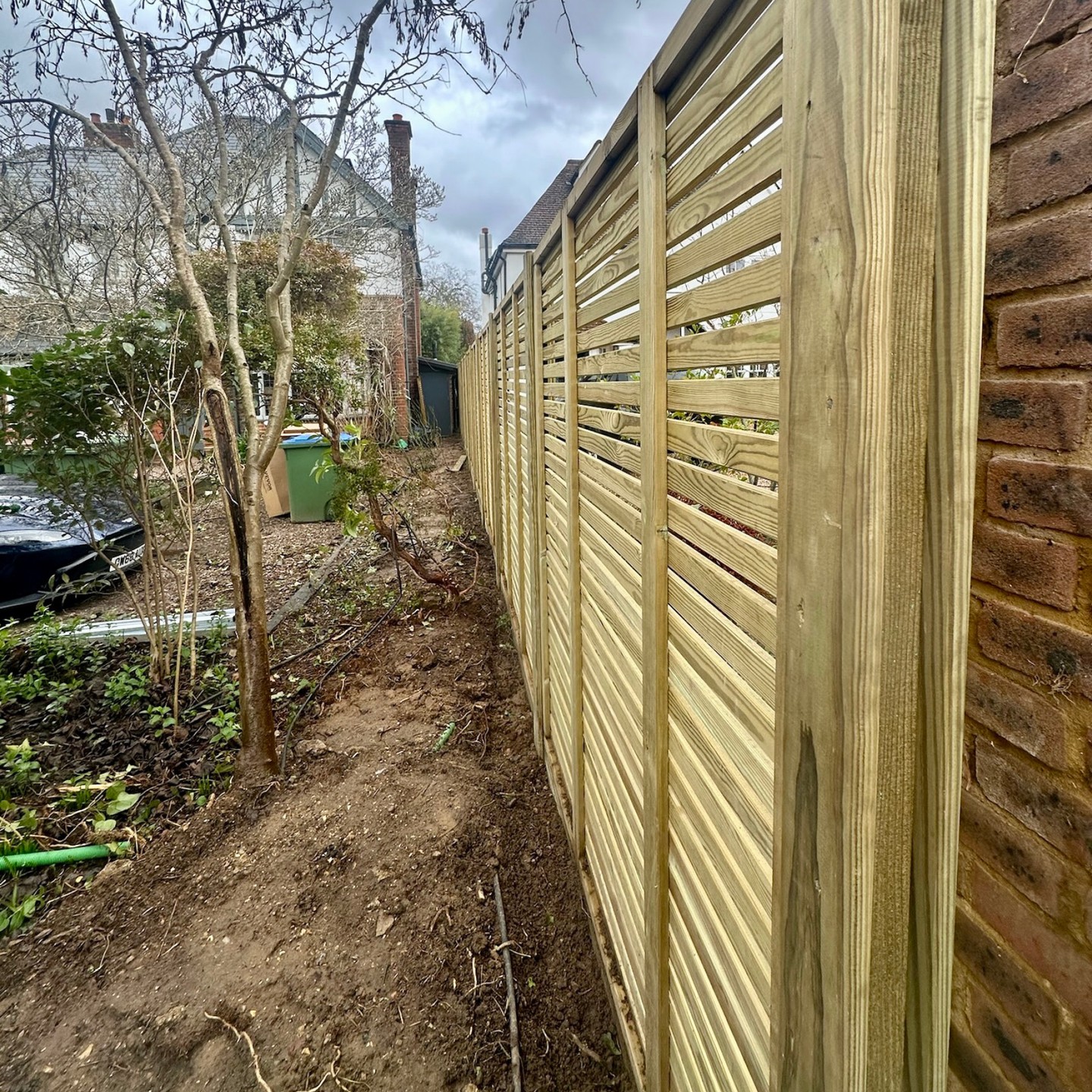Horizontal slatted fence panels and timber posts set against a brick boundary wall in East Molesey