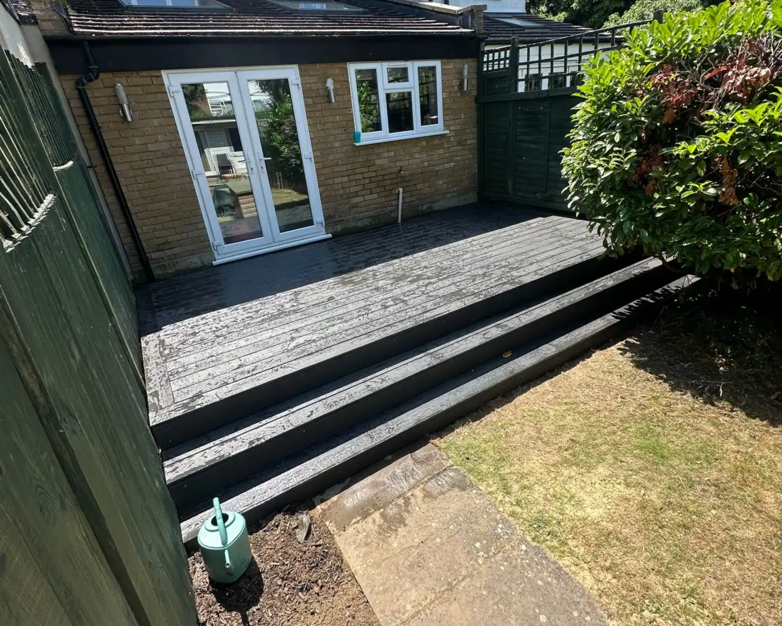 Charcoal composite decking with full width steps down to the lawn at a house in Teddington