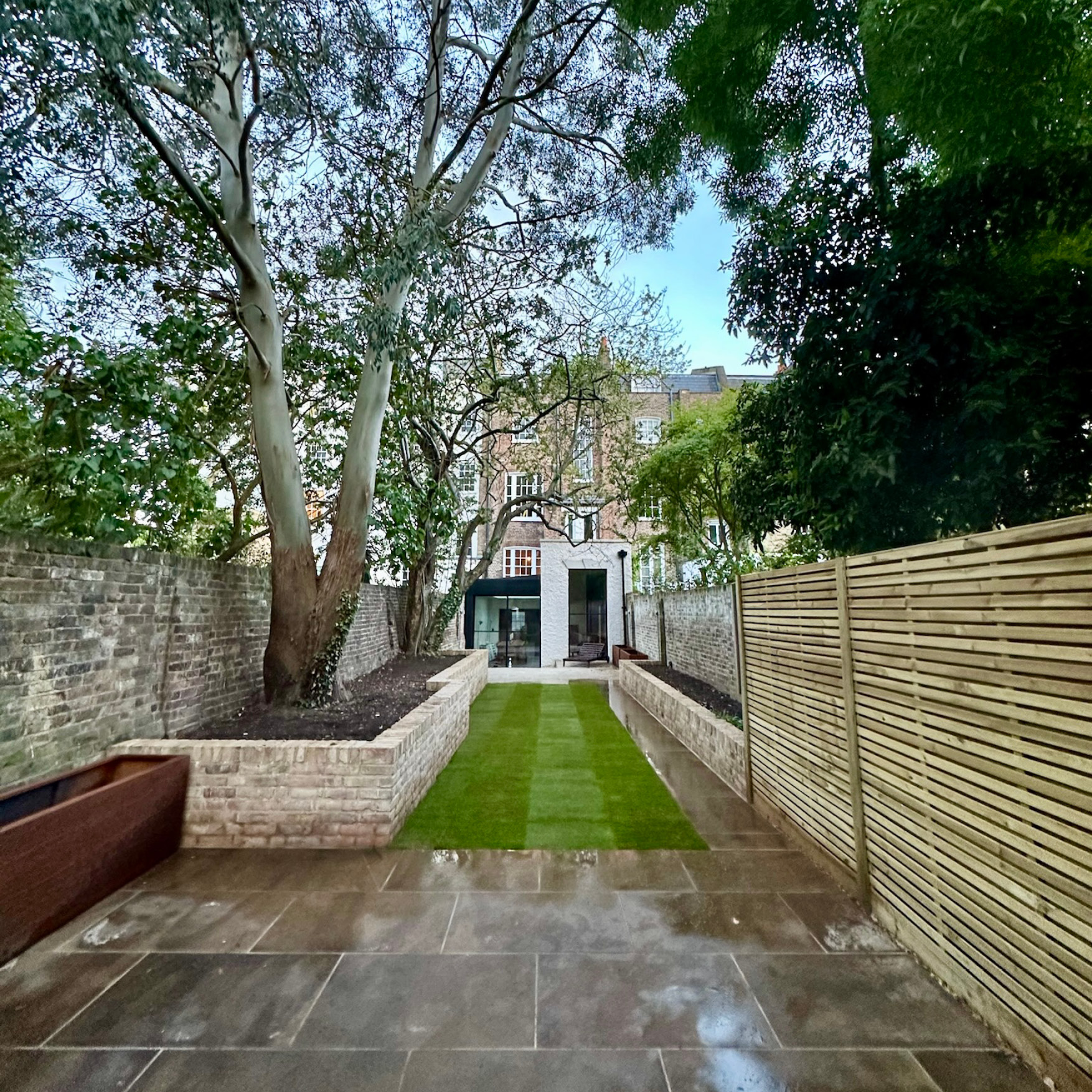 Islington walled garden with a new central lawn, stone paving, raised brick beds and slatted fencing