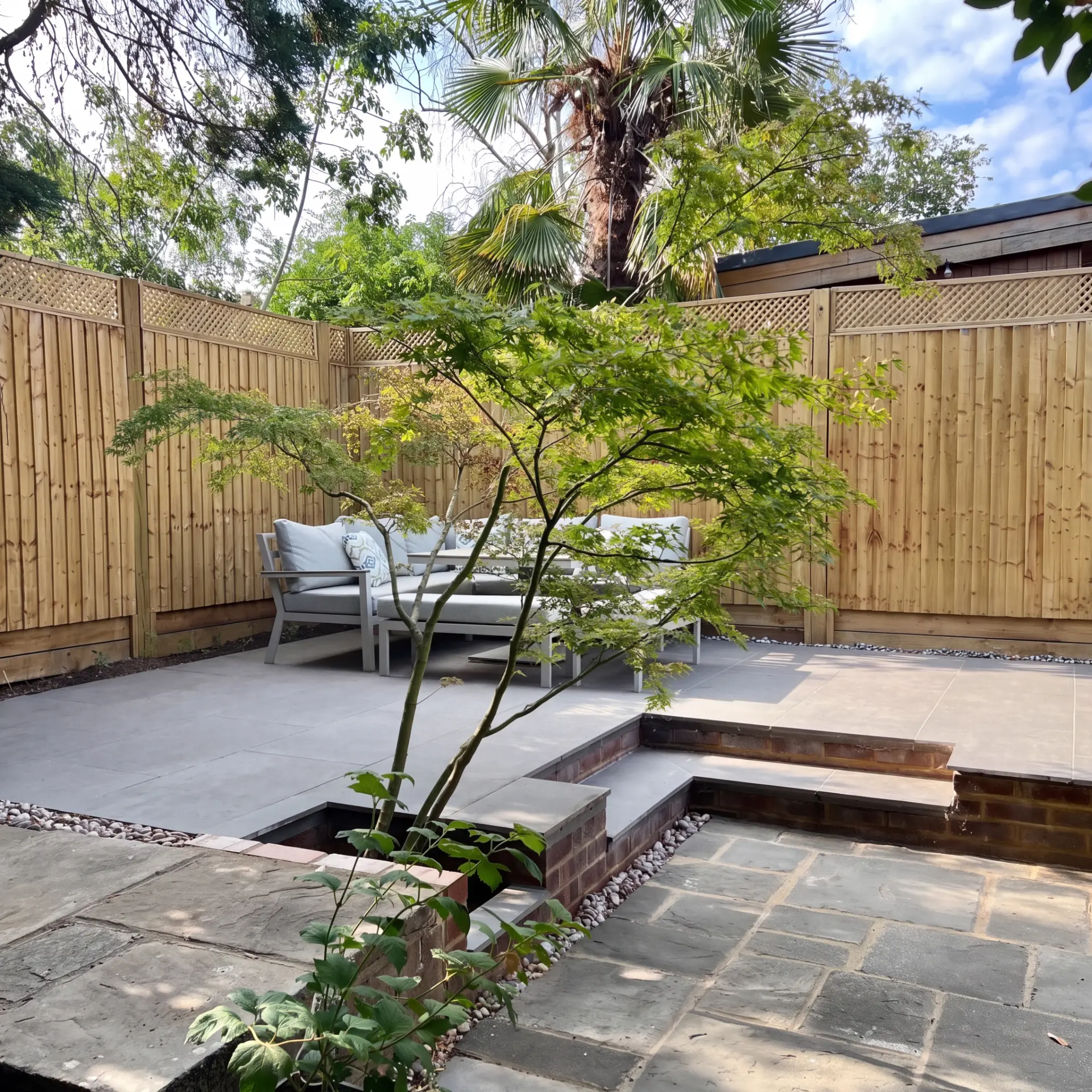 Finished East Molesey garden transformation with porcelain patio, outdoor seating, new close board fencing and retained mature trees