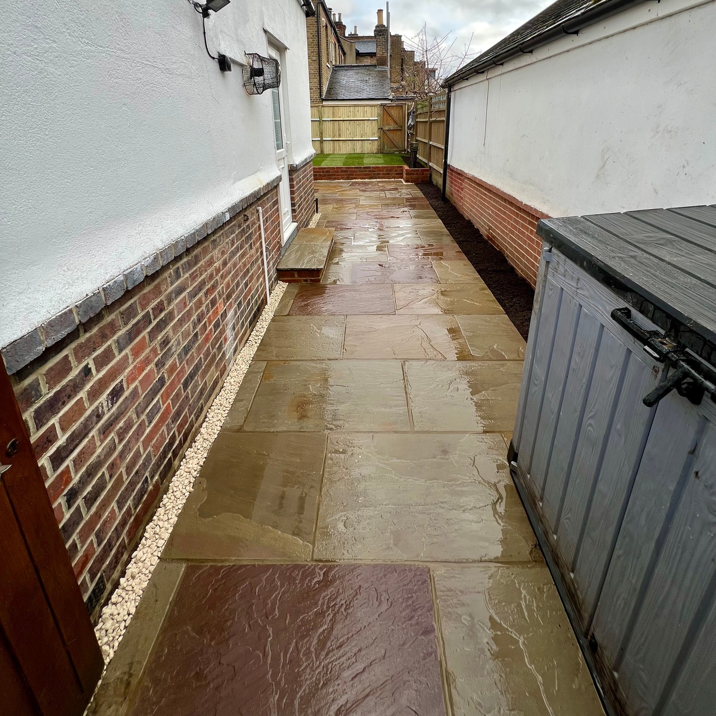 After: side return paved in Indian sandstone with a gravel margin along the brick wall